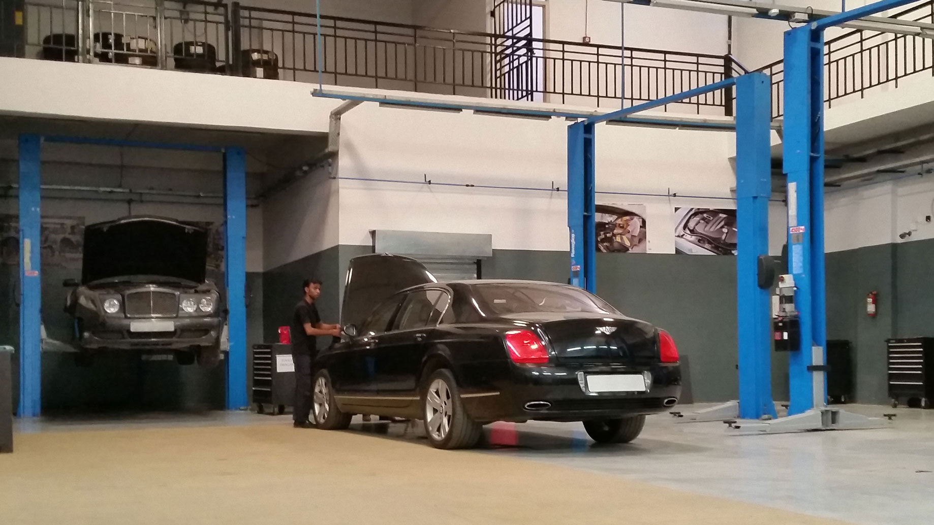 Young mechanic works on two black Bentleys being serviced at his workshop