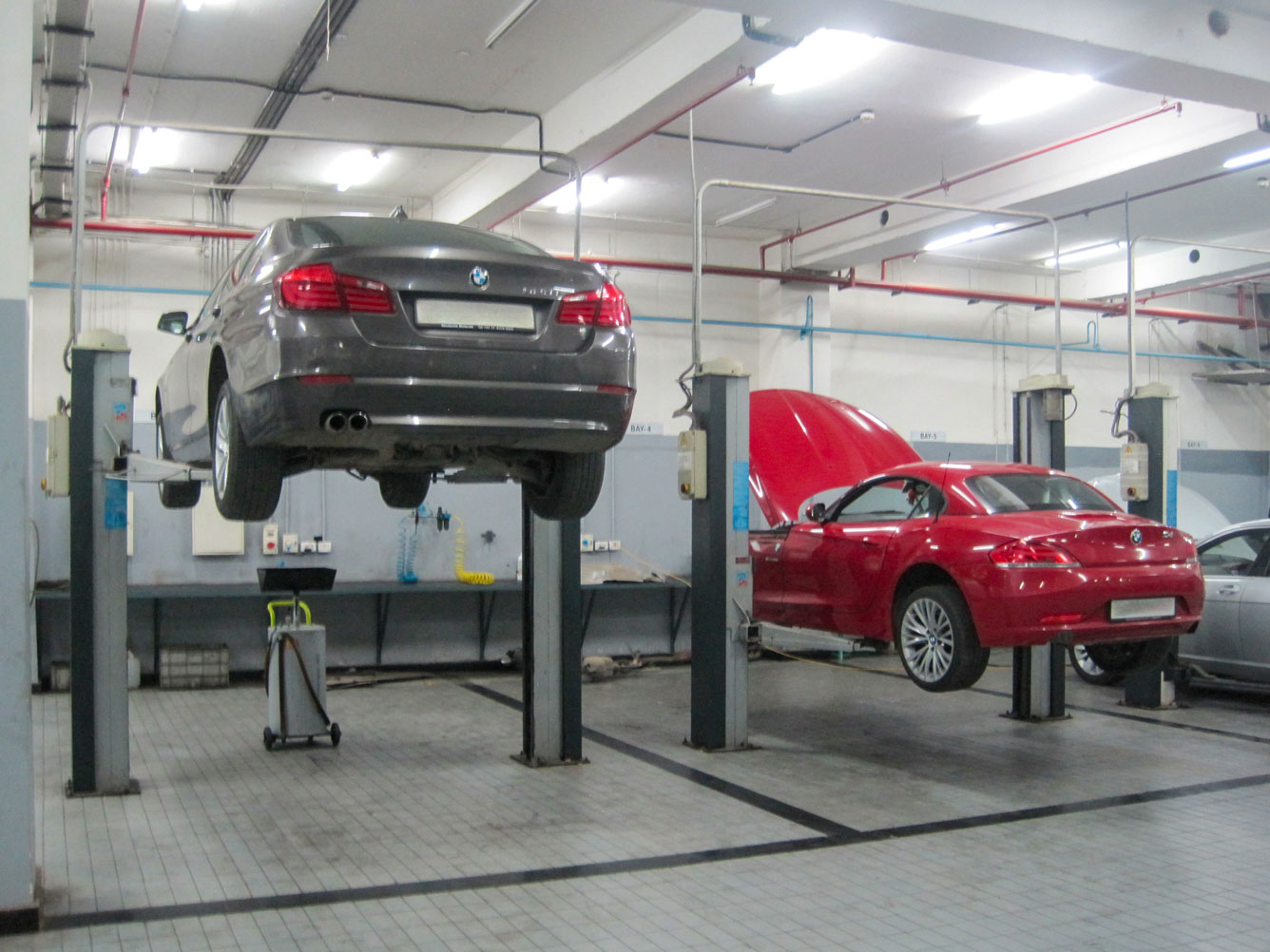 A grey and a red BMW are lifted by a pair of workshop lifts in a workshop