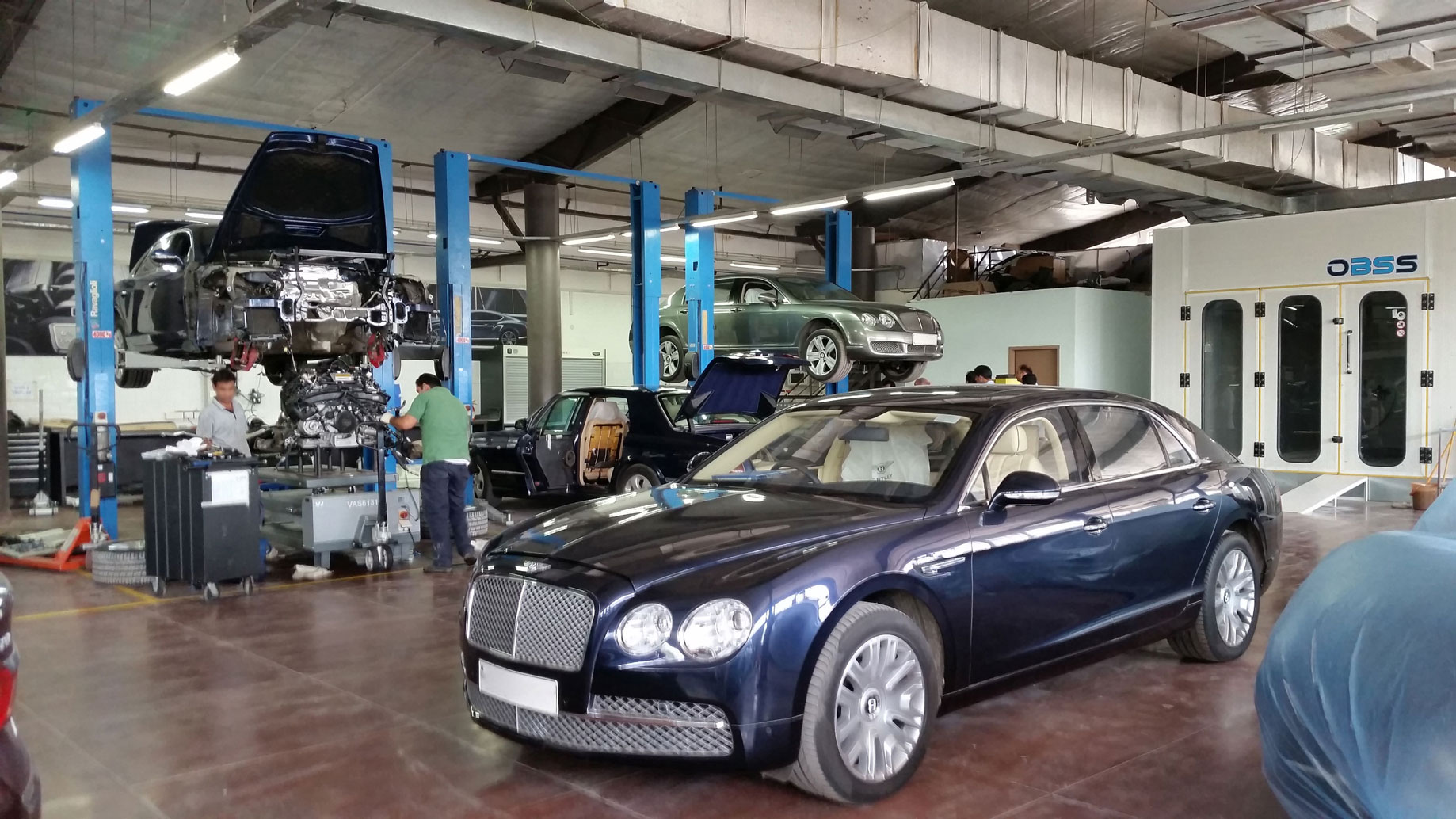 Blue Bentley parked in a garage where other repairs are carried out behind it